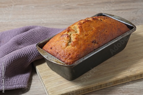 Freshly baked banana bread in baking tin on wooden board photo