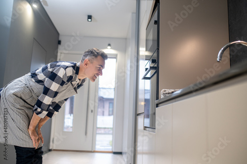 Man sideways to camera leaning towards oven watching