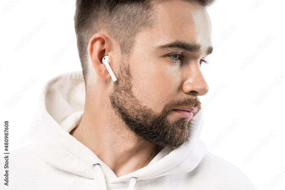 Obraz premium Handsome bearded man in white clothes using wireless earbuds on white background