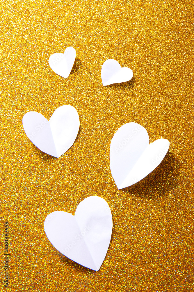 Obraz premium Valentine's Day background. White volumetric paper hearts on golden background. Valentine's Day concept. Vertical flat lay