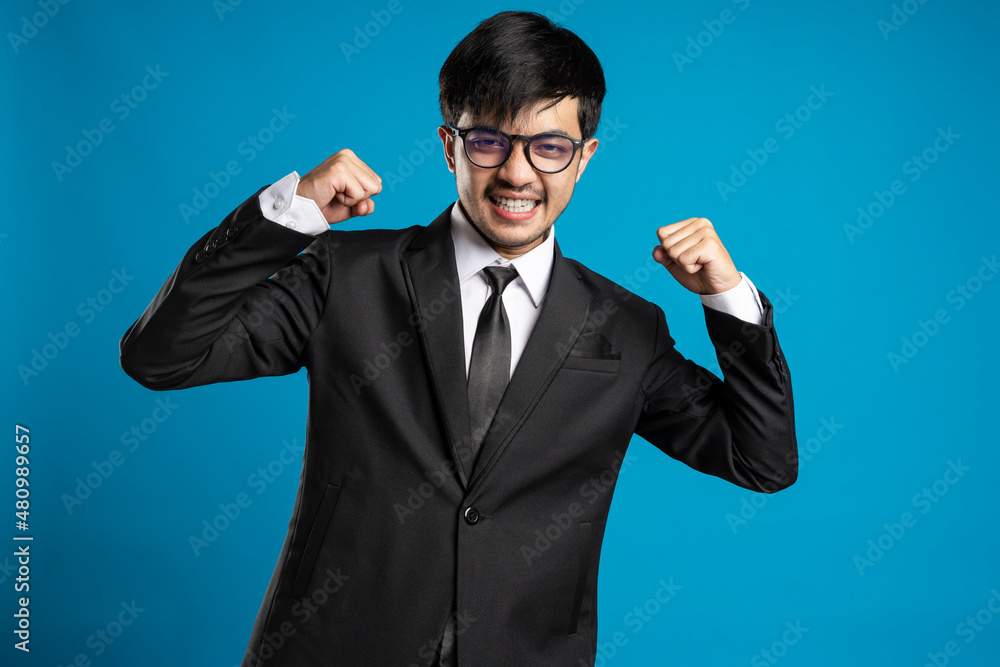 Portrait of excited man with opened mouth dressed in formal wear giving fist against blue background Portrait of excited man with opened mouth dressed in formal wear giving fist against blue background