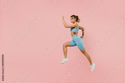 Full body young strong sporty athletic fitness trainer instructor woman wear blue tracksuit spend time in home gym jump high run isolated on pastel plain light pink background. Workout sport concept.