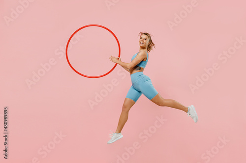 Full body young strong sporty athletic fitness trainer instructor woman wear blue tracksuit spend time in home gym hold hula hoop isolated on pastel plain light pink background. Workout sport concept. © ViDi Studio