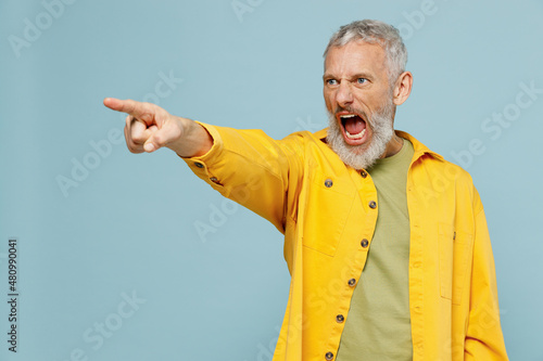 Elderly angry strict indignant gray-haired mustache bearded man 50s wear yellow shirt point index finger aside scream isolated on plain pastel light blue background studio. People lifestyle concept. photo