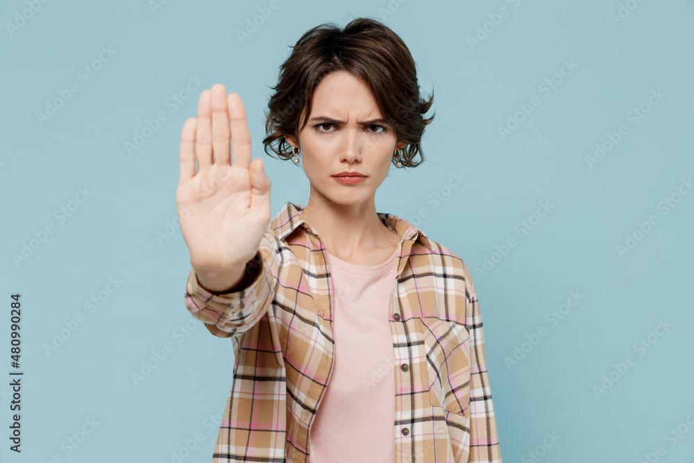 Young serious strict sad caucasian woman 20s wearing casual brown shirt showing stop gesture with palm isolated on pastel plain light blue color background studio portrait. People lifestyle concept. Young serious strict sad caucasian woman 20s wearing casual brown shirt showing stop gesture with palm isolated on pastel plain light blue color background studio portrait. People lifestyle concept.