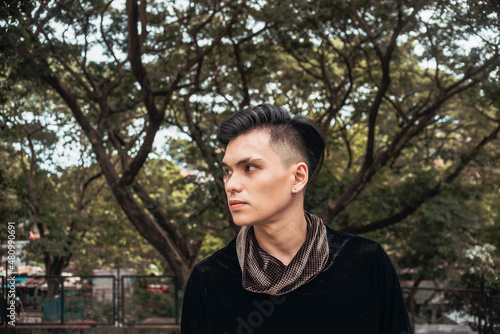 A handsome yet enigmatic young man with a straight-face looking away. Outdoor scene at a park.