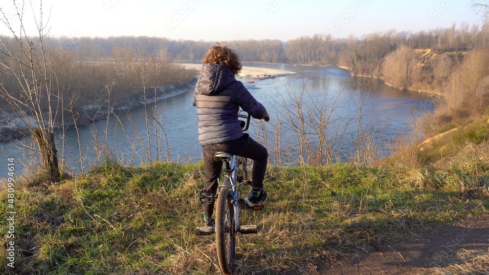 7 years old boy child drives a bicycle in nature wood near the river in Ticino natural park , Pavia Italy, Europe