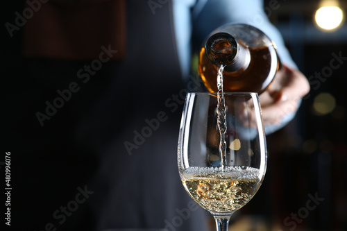 Bartender pouring white wine from bottle into glass indoors, closeup. Space for text photo