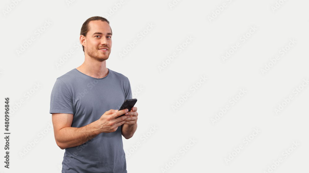 Blonde unshaven man holds a mobile phone in his hands and looks into the camera smiling Blonde unshaven man holds a mobile phone in his hands and looks into the camera smiling
