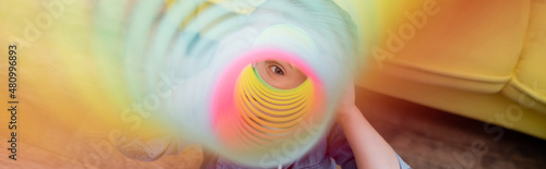 Quadro su tela Child looking at camera through colorful slinky at home, banner.