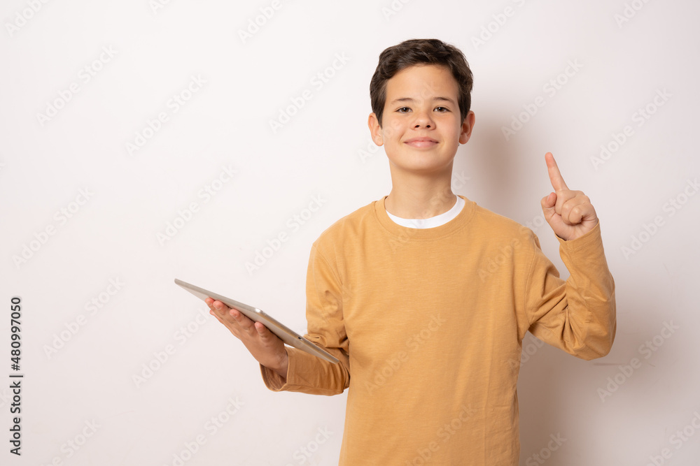 Cute boy in casual t-shirt holding tablet pointing finger up over white background. Cute boy in casual t-shirt holding tablet pointing finger up over white background.