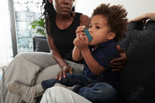 Worried mother looking at little son holding inhaler to treat asthmatic attack photo