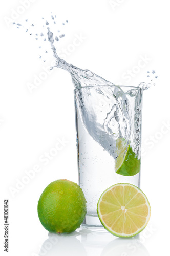 Pure water splashing out of glass and fresh limes on white background