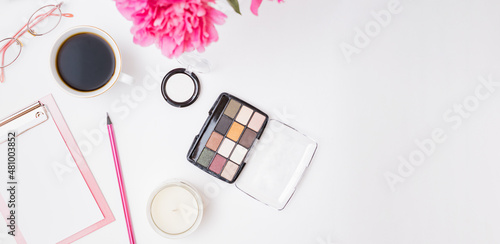 Fashion blogger workspace with blank paper clipboard, glasses, cup of coffee, pencil and pink peonies on a white table. Flat lay banner or shop header with makeup cosmetic products