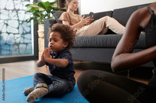 Little boy breathing out when sitting on yoga mat in lotus position just like his mother