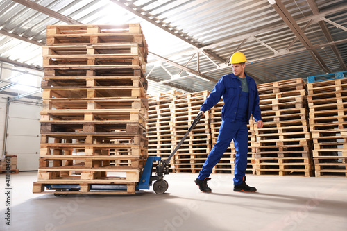 Foto Worker moving wooden pallets with manual forklift in warehouse