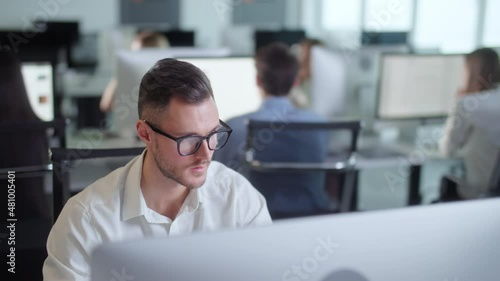 Serious Young Man Working on Decktop Computer While Working in Big Open Space Office. Portrait of Positive Business Man Looking at Computer Screen Indoors.