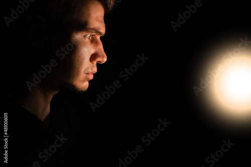 The head of a young European male looks at the light in the dark on a black isolated background. Side view 
