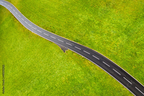 A straight road in a green meadow. Asphalt and grass. An aerial landscape fro...