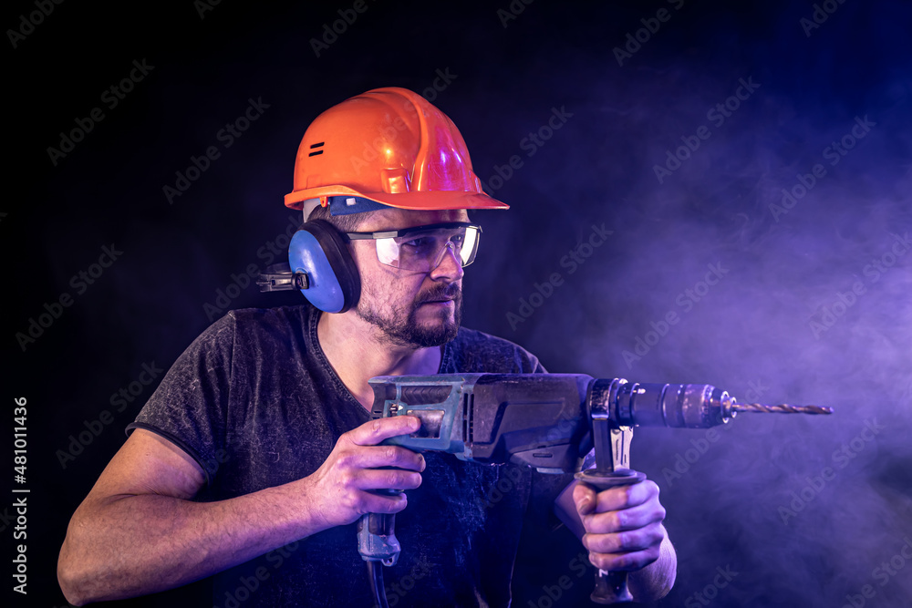 Fototapeta premium A young man in overalls protective helmet hard hat hold electric drill.