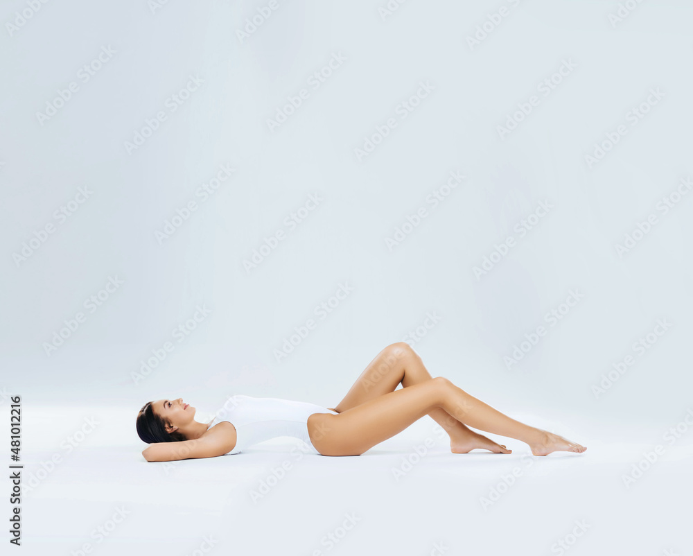 Obraz premium Young, fit and beautiful brunette woman in white swimsuit posing in studio. Concept of fitness, dieting and skin care.