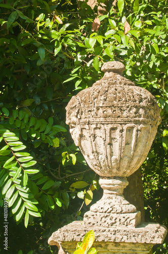 Front view, close distance, of a cut stone jar with cover, on corner of a stone wall, with green vegetation