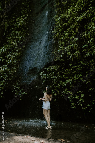 A young female traveller exploring waterfall in Bali. Nature  green lush tropical landscapes  water  woman