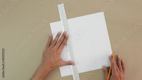 Trace a 3x3 grid on white cardboard. Craft paper background. Ruler and pencil are used. Brown hands. School activity. 