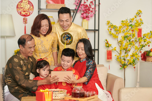 Portrait of happy threee generation family in ao dai dresses at Chinere New Year party video calling friends photo