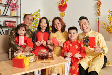 Smiling family members in ao dai dresses holding red lucky money envelopes