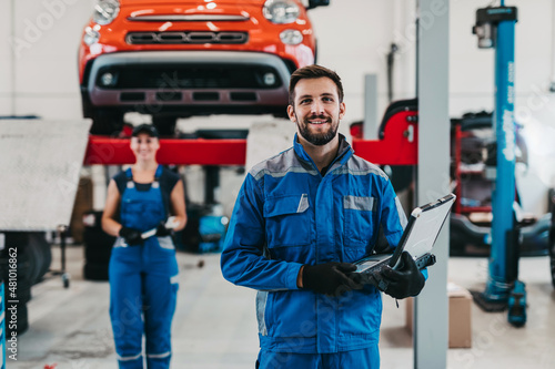 Male and female mechanics working together in large modern car repair service.