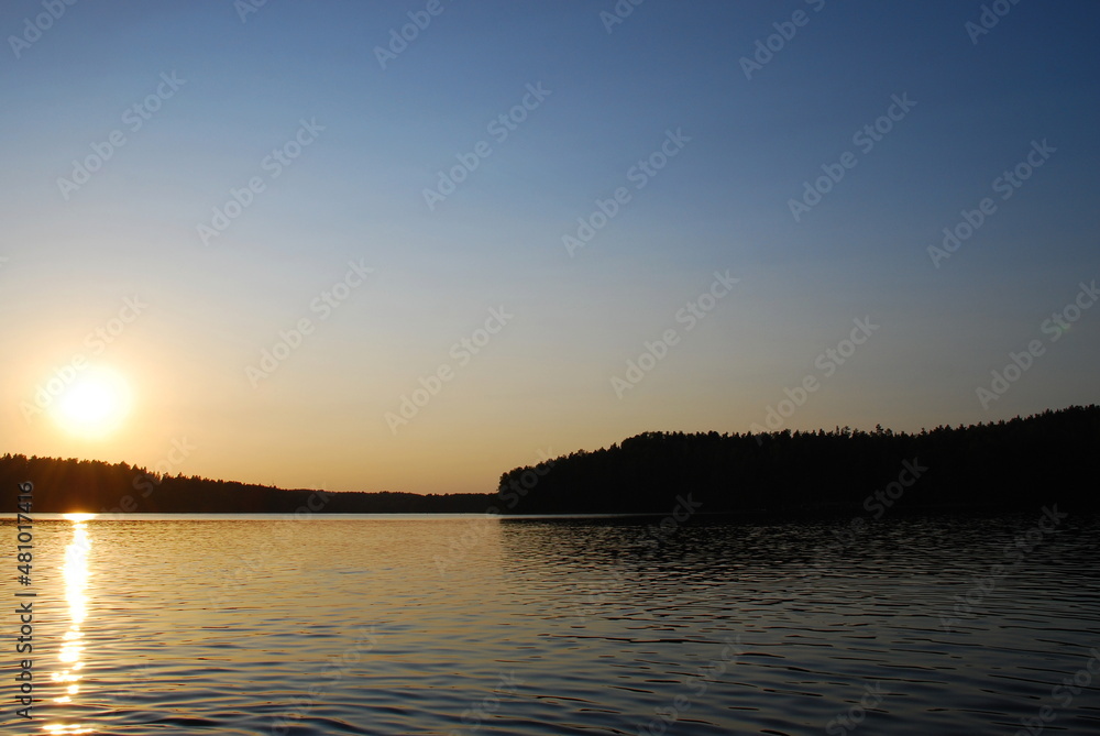 Beautiful sunset on the shore of a forest lake. The sun went down low over the forest growing on the shore of the lake. The surface of the water is almost smooth, the sun's rays are reflected from it.