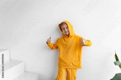 a teenager in a yellow tracksuit on a monochrome background in a hood shows super