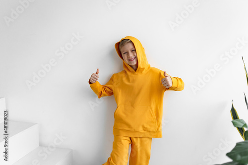 a teenager in a yellow tracksuit on a monochrome background in a hood shows super