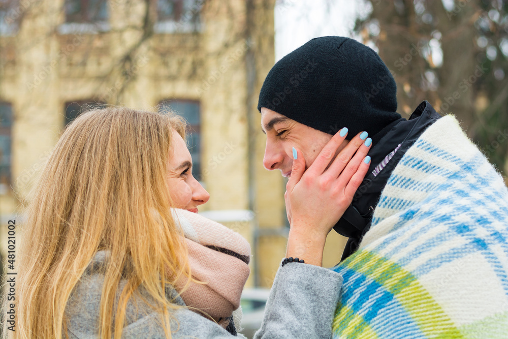 Loving couple in a blanket in winter. The guy hugs a girl on the street in winter.