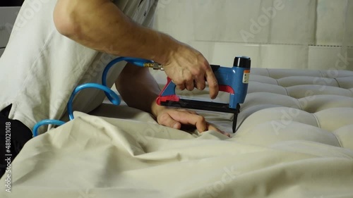 Man upholster part of the bed with a new fabric using a furniture stapler