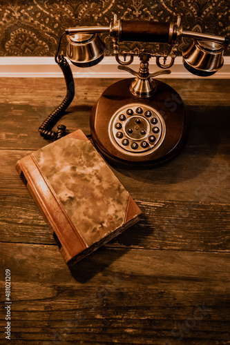 Old School rotary phone with brass details on dark wood table with brown leatherbound book