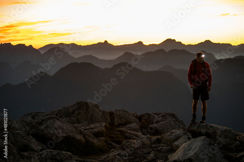 Mountaineer reaches summit at dawn, headlamp on. photo