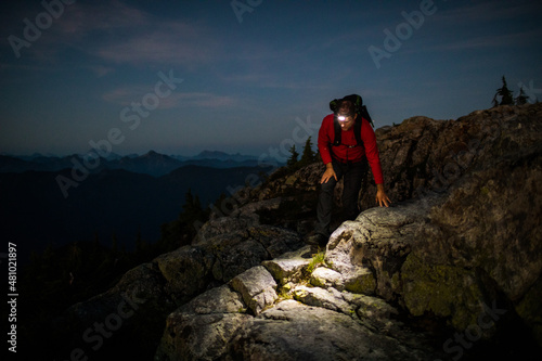 Backpacker carefully hikes rocky summit at night with headlamp photo