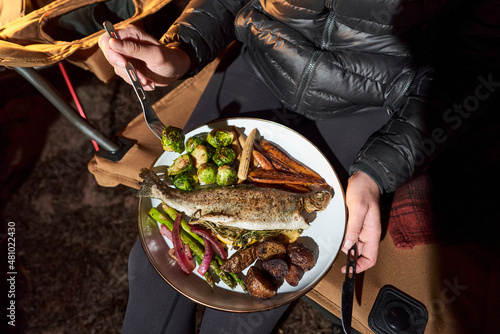 Woman has camp dinner with trout, brussel sprouts and carrots.