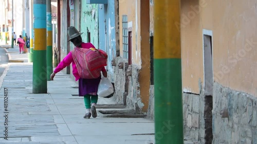 Traditionally dressed Peruvian woman walks through the street of an andean village with a lot of luggage. photo