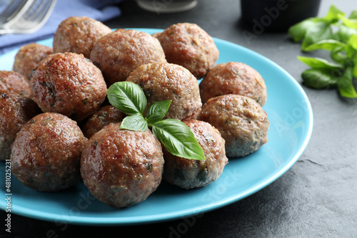 Tasty cooked meatballs with basil on black table, closeup