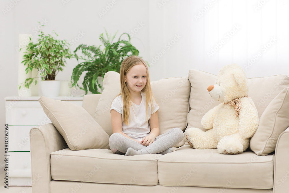 Photo of little girl in white clothes sitting on white sofa with teddy bear. Photo of little girl in white clothes sitting on white sofa with teddy bear.