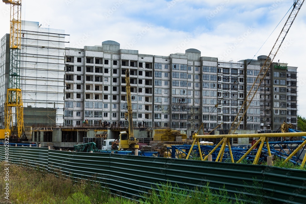 Large construction site including several cranes working on a building complex, with clear blue sky and the sun Large construction site including several cranes working on a building complex, with clear blue sky and the sun