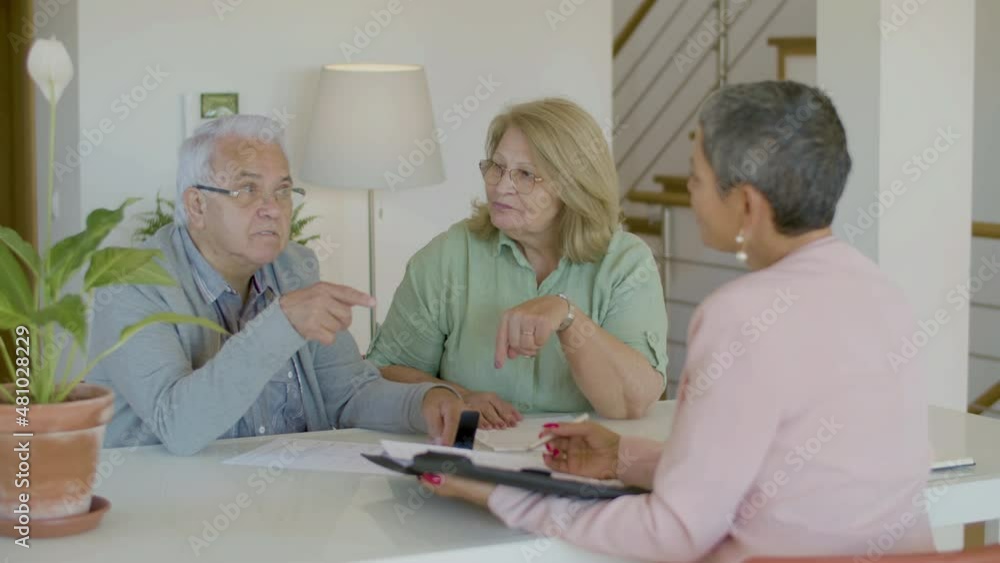 Senior couple talking with realtor while sitting at table. Elderly man and women in eyeglasses having negotiations with real estate agent, discussing details of agreement. Real estate purchase concept Senior couple talking with realtor while sitting at table. Elderly man and women in eyeglasses having negotiations with real estate agent, discussing details of agreement. Real estate purchase concept
