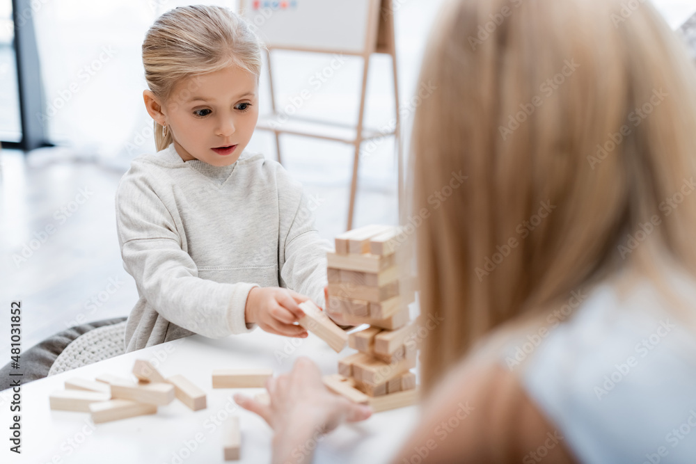 Girl holding wooden block while playing with blurred mother at home. Girl holding wooden block while playing with blurred mother at home.
