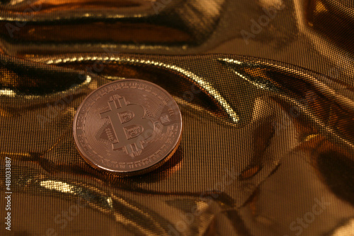 Copper colored physical bitcoin in front of golden background that looks like molten metal or gold, narrow depth of field, focus on coin