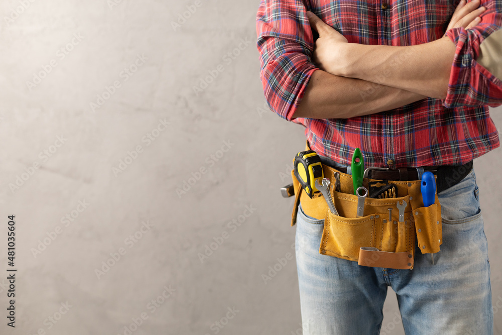 Worker man with tool belt near concrete or cement wall. Male hand and tools for house renovation - obrazy, fototapety, plakaty 