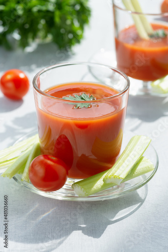 Two glasses with fresh tomato juice, celery, parsley and ripe tomatoes on light background