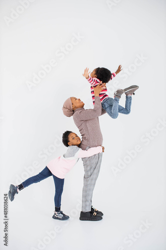 Positive african american islamic woman and her two little daughters spending free time with fun and pleasure in studio. Isolated over white background.